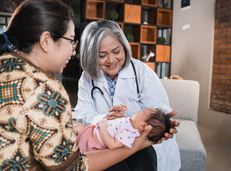 doctor examines a small baby while being held by his mother