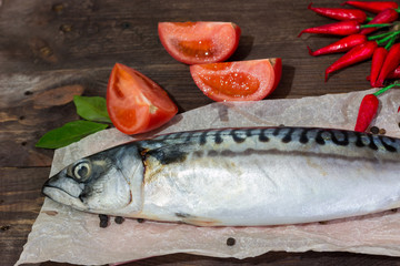 Raw mackerel fish with tomatoes, chili peppers on a dark wooden table. Ingredients for cooking dinner. Healthy eating