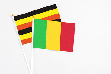 Mali and Uganda stick flags on white background. High quality fabric, miniature national flag. Peaceful global concept.White floor for copy space.