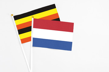 Netherlands and Uganda stick flags on white background. High quality fabric, miniature national flag. Peaceful global concept.White floor for copy space.