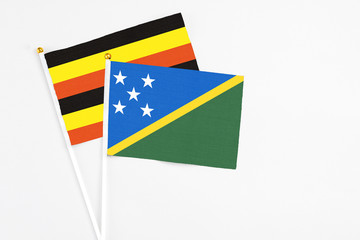 Solomon Islands and Uganda stick flags on white background. High quality fabric, miniature national flag. Peaceful global concept.White floor for copy space.