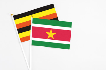 Suriname and Uganda stick flags on white background. High quality fabric, miniature national flag. Peaceful global concept.White floor for copy space.