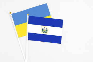 El Salvador and Ukraine stick flags on white background. High quality fabric, miniature national flag. Peaceful global concept.White floor for copy space.