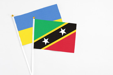 Saint Kitts And Nevis and Ukraine stick flags on white background. High quality fabric, miniature national flag. Peaceful global concept.White floor for copy space.