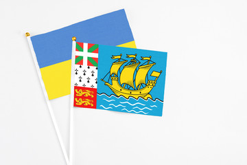 Saint Pierre And Miquelon and Ukraine stick flags on white background. High quality fabric, miniature national flag. Peaceful global concept.White floor for copy space.