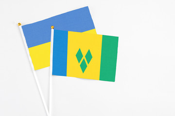 Saint Vincent And The Grenadines and Ukraine stick flags on white background. High quality fabric, miniature national flag. Peaceful global concept.White floor for copy space.