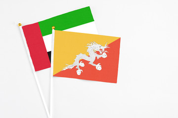 Bhutan and United Arab Emirates stick flags on white background. High quality fabric, miniature national flag. Peaceful global concept.White floor for copy space.