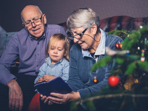 Grandparents and toddler looking at smartphone by christmas tree