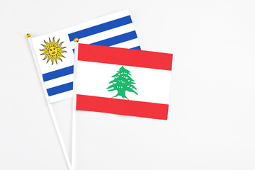 Lebanon and Uruguay stick flags on white background. High quality fabric, miniature national flag. Peaceful global concept.White floor for copy space.