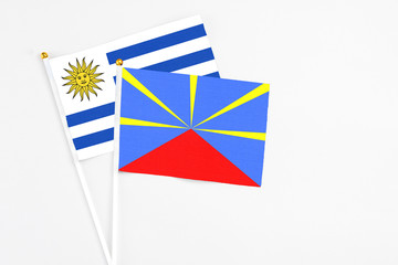 Reunion and Uruguay stick flags on white background. High quality fabric, miniature national flag. Peaceful global concept.White floor for copy space.