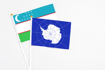 Antarctica and Uzbekistan stick flags on white background. High quality fabric, miniature national flag. Peaceful global concept.White floor for copy space.