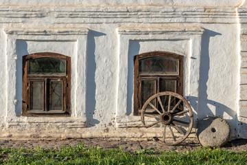 Fototapeta premium The facade of an ancient house near which there is an old wheel from a cart and a millstone from an ancient mill