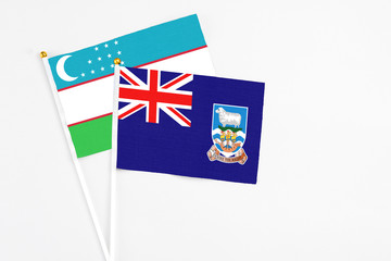 Fototapeta premium Falkland Islands and Uzbekistan stick flags on white background. High quality fabric, miniature national flag. Peaceful global concept.White floor for copy space.