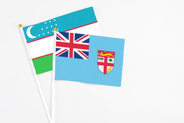 Fiji and Uzbekistan stick flags on white background. High quality fabric, miniature national flag. Peaceful global concept.White floor for copy space.