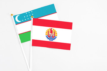 French Polynesia and Uzbekistan stick flags on white background. High quality fabric, miniature national flag. Peaceful global concept.White floor for copy space.