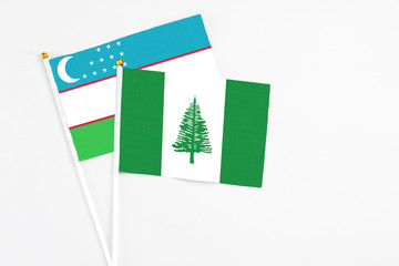 Norfolk Island and Uzbekistan stick flags on white background. High quality fabric, miniature national flag. Peaceful global concept.White floor for copy space.