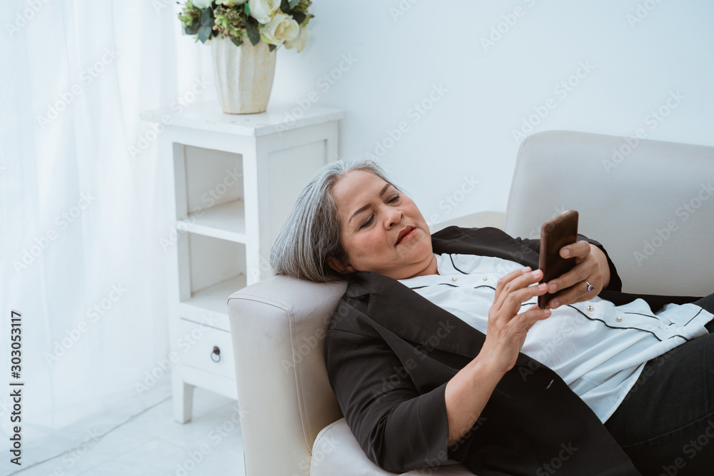 Wall mural Old woman confident lying on the couch when using a mobile phone