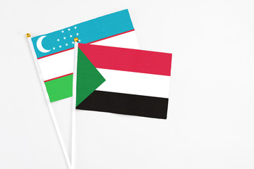 Sudan and Uzbekistan stick flags on white background. High quality fabric, miniature national flag. Peaceful global concept.White floor for copy space.