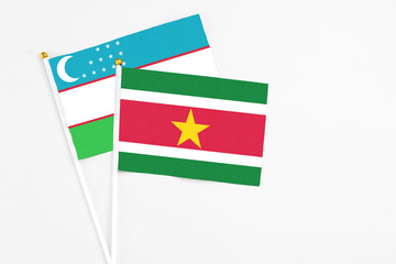 Suriname and Uzbekistan stick flags on white background. High quality fabric, miniature national flag. Peaceful global concept.White floor for copy space.