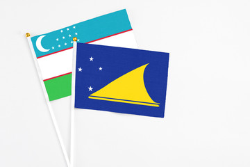 Tokelau and Uzbekistan stick flags on white background. High quality fabric, miniature national flag. Peaceful global concept.White floor for copy space.