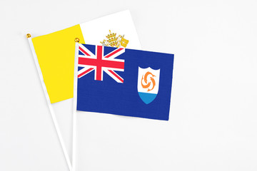 Fototapeta premium Anguilla and Vatican City stick flags on white background. High quality fabric, miniature national flag. Peaceful global concept.White floor for copy space.
