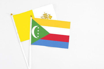 Comoros and Vatican City stick flags on white background. High quality fabric, miniature national flag. Peaceful global concept.White floor for copy space.