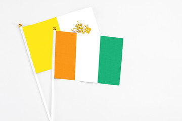 Cote D'Ivoire and Vatican City stick flags on white background. High quality fabric, miniature national flag. Peaceful global concept.White floor for copy space.