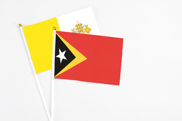 East Timor and Vatican City stick flags on white background. High quality fabric, miniature national flag. Peaceful global concept.White floor for copy space.
