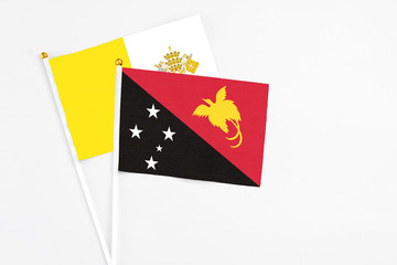 Papua New Guinea and Vatican City stick flags on white background. High quality fabric, miniature national flag. Peaceful global concept.White floor for copy space.