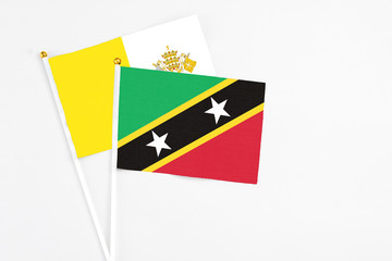 Fototapeta premium Saint Kitts And Nevis and Vatican City stick flags on white background. High quality fabric, miniature national flag. Peaceful global concept.White floor for copy space.