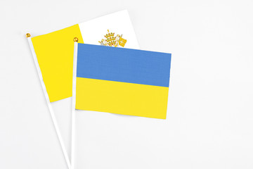 Ukraine and Vatican City stick flags on white background. High quality fabric, miniature national flag. Peaceful global concept.White floor for copy space.