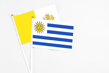 Uruguay and Vatican City stick flags on white background. High quality fabric, miniature national flag. Peaceful global concept.White floor for copy space.