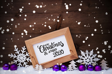 Fototapeta na wymiar Frame With English Calligraphy Merry Christmas And A Happy 2020. Pruple Christmas Ornament Like Ball, Tree And Star. Wooden Background With Snow