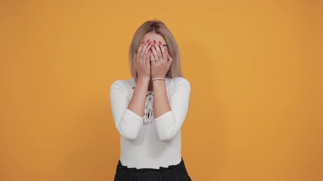 Caucasian attractive girl over orange wall making unimportant gesture while lifting the shoulders wearing pastel white shirt