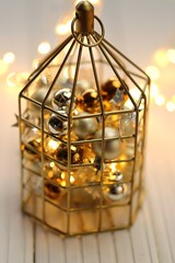 Christmas and New Year  decor. Golden cage with golden and silver balls and a shining garland on a white table. Christmas time.