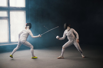 A fencing training - two women in protective costumes having a duel