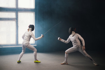 A fencing training in the studio - two women in white protective costumes having a duel