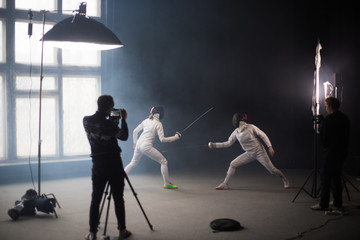 A fencing training in the studio - two women in protective costumes having a duel - a cameraman...
