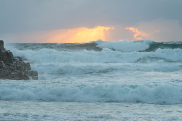 Sun rising over the horizon at a beach by a headland