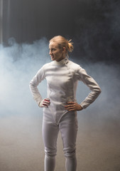 A young smiling woman fencer standing in the dark smoky studio