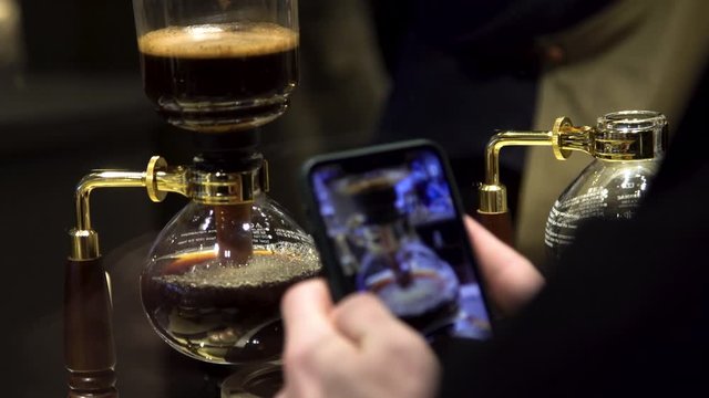 close up view of a man taking photos with his smart phone of coffee being brewed at the local Starbucks in Chicago  while the barista is serving coffee drinks to customers