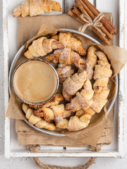 A cup of coffe and homemade crescent rolls (croissant) on plate with cinnamon sticks, white christmas backround , top view