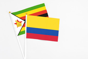 Colombia and Zimbabwe stick flags on white background. High quality fabric, miniature national flag. Peaceful global concept.White floor for copy space.