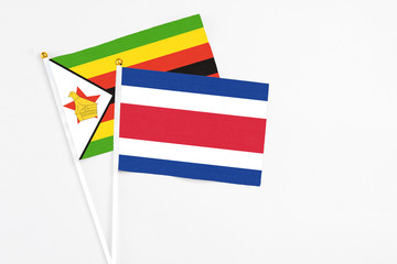 Costa Rica and Zimbabwe stick flags on white background. High quality fabric, miniature national flag. Peaceful global concept.White floor for copy space.