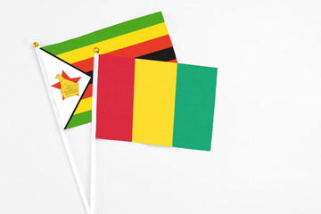 Guinea and Zimbabwe stick flags on white background. High quality fabric, miniature national flag. Peaceful global concept.White floor for copy space.