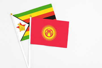 Kyrgyzstan and Zimbabwe stick flags on white background. High quality fabric, miniature national flag. Peaceful global concept.White floor for copy space.