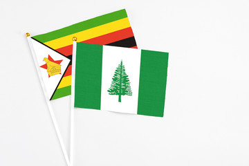 Norfolk Island and Zimbabwe stick flags on white background. High quality fabric, miniature national flag. Peaceful global concept.White floor for copy space.