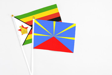Reunion and Zimbabwe stick flags on white background. High quality fabric, miniature national flag. Peaceful global concept.White floor for copy space.