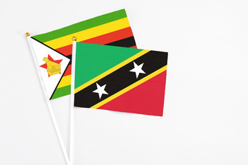 Saint Kitts And Nevis and Zimbabwe stick flags on white background. High quality fabric, miniature national flag. Peaceful global concept.White floor for copy space.