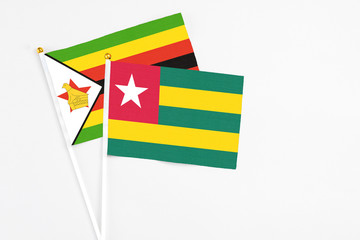 Togo and Zimbabwe stick flags on white background. High quality fabric, miniature national flag. Peaceful global concept.White floor for copy space.
